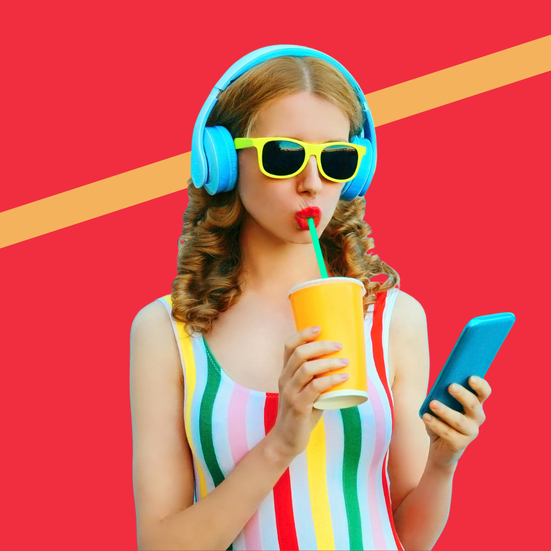 Girl in colourful top wearing blue headphones, drinking a smoothie, looking at phone